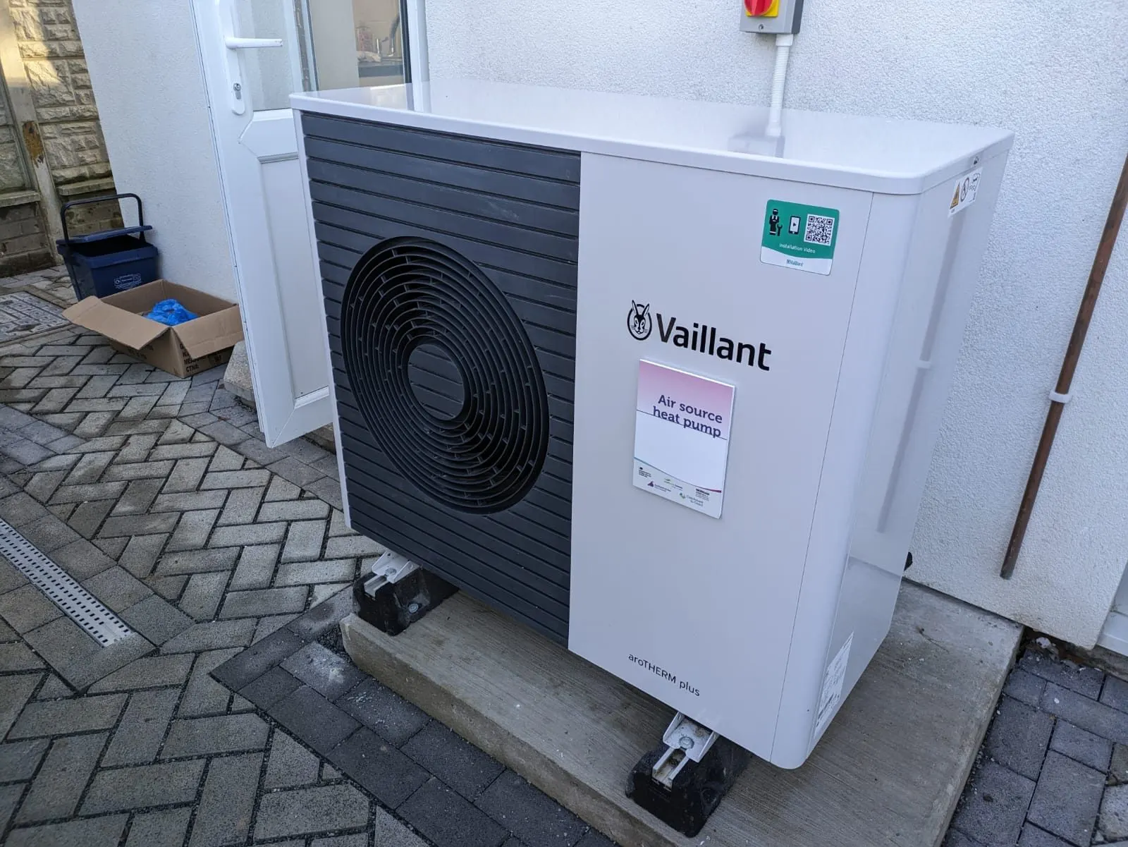 Pompe à chaleur air-eau monobloc sur un socle en béton, contre le mur enduit d'une maison mitoyenne